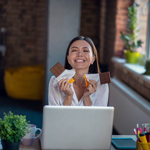 Lächelnde Frau mit zwei Tafeln Schokolade vor Laptop